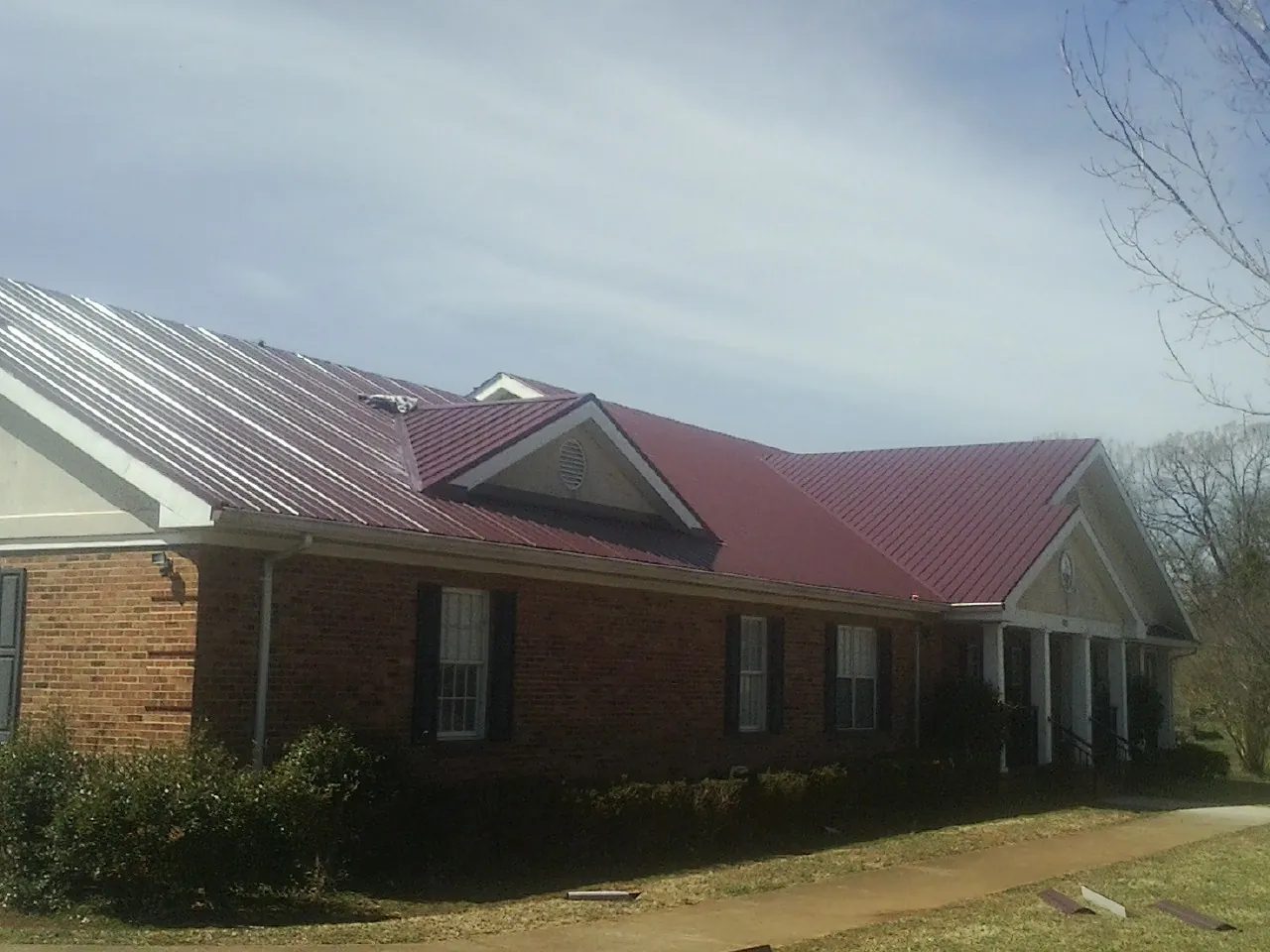 Red metal roof with gabled entries on a long brick building, from a Hail Damage Roof Repair job in Patterson
